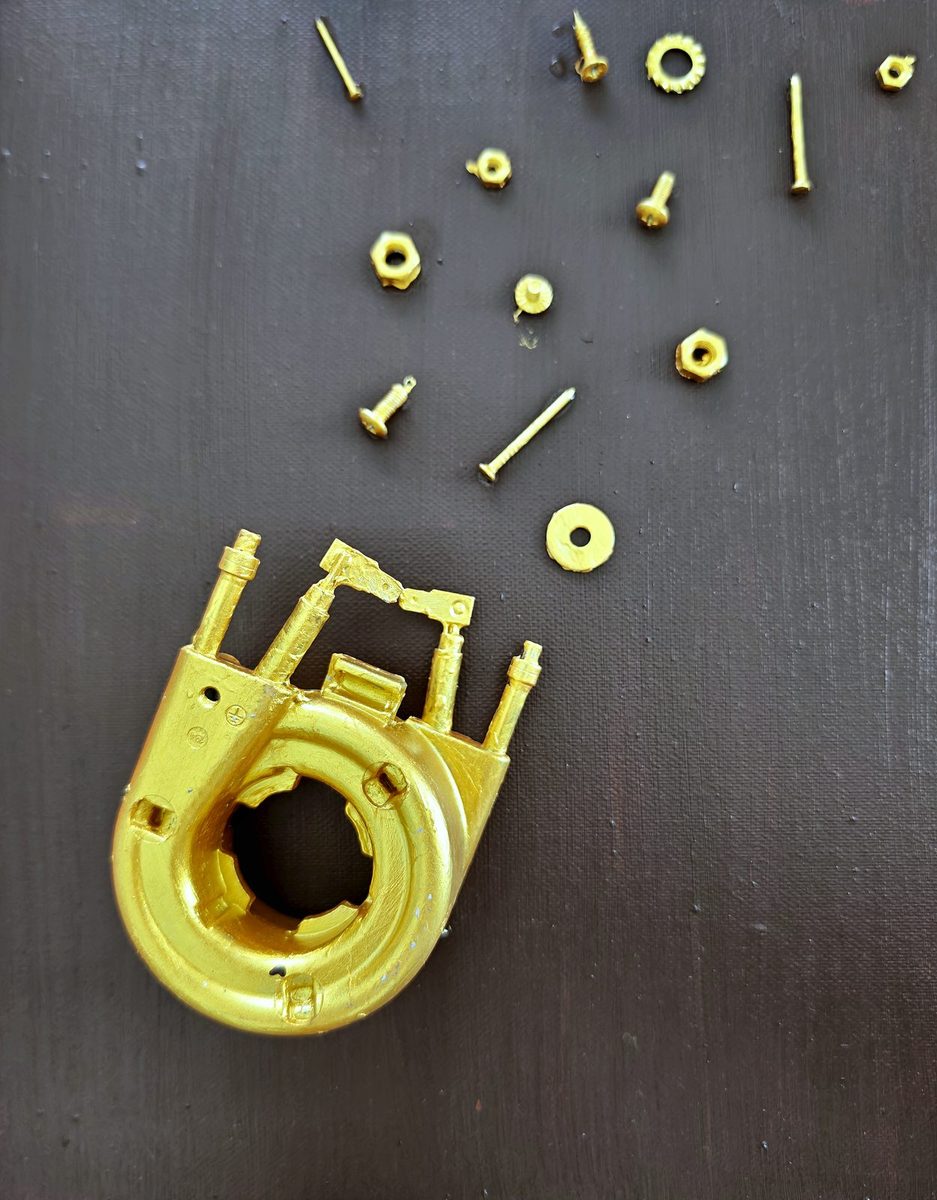 Gilded mechanical parts, screws and nuts scattered across a black canvas